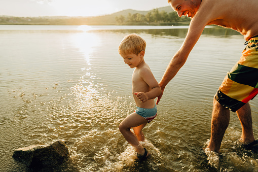Photo of a father and son, splashing feet and playing in the lake; enjoying summer days far from the city hustle.