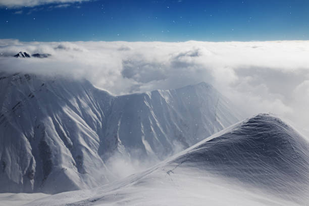 istock High snowy mountains covered with beautiful sunlight clouds and fog in snowfall 1266685047