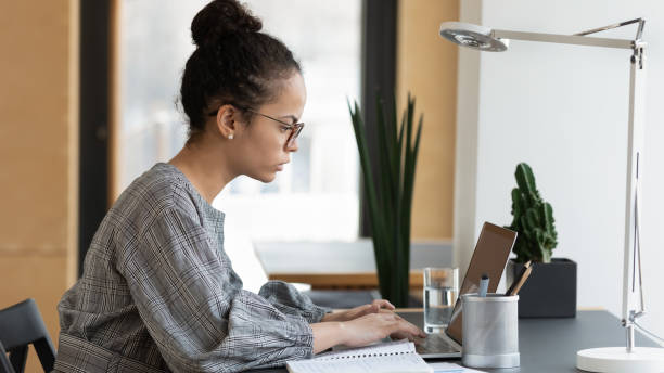 istock Focused ethnic woman work on laptop preparing report 1266690388