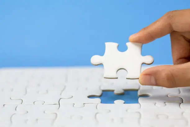 Photo of Hand put the last piece of jigsaw puzzle to complete the mission. Completing final task, missing jigsaw puzzle pieces and business concept with a puzzle piece missing.