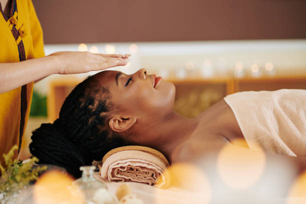 Healing reiki session Therapist holding hands over head of pretty young Black woman to transfer energy during healing reiki session indulgence stock pictures, royalty-free photos & images