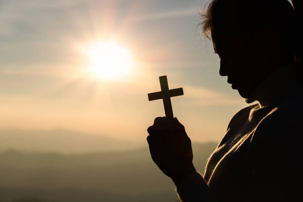 istock human hands praying to the GOD while holding a crucifix symbol with bright sunbeam. 1266702813