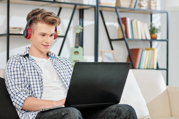 Teenage boy playing on laptop Teenage boy listening to music in headphones when working or playing game on laptop home schooling homework computer learning stock pictures, royalty-free photos & images