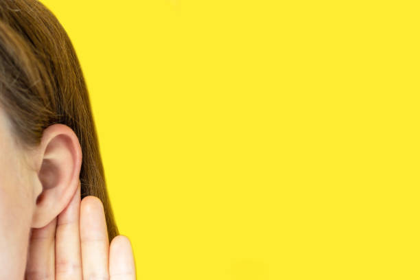 istock Young beautiful girl holds ear on yellow background, copy space 1266717849