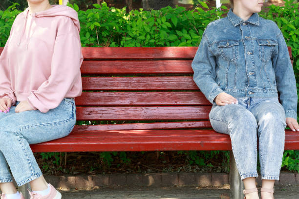 istock Two girls sit on bench keeping their distance, view from the front 1266725555