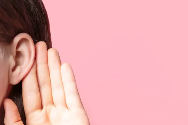 Photo of The girl listens attentively with her palm to her ear close-up on pink background