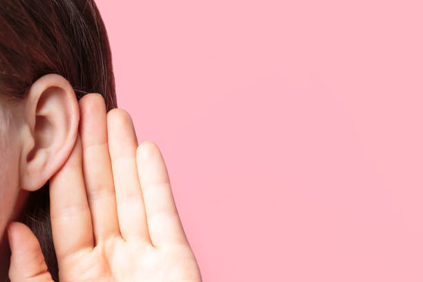 the girl listens attentively with her palm to her ear close-up on pink background - attentively imagens e fotografias de stock