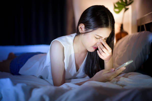 Woman is feeling eye pain when using smart phone at night stock photo