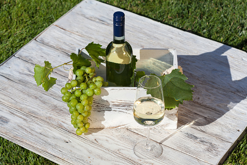 White wine on wooden white vintage table with green lawn on background
