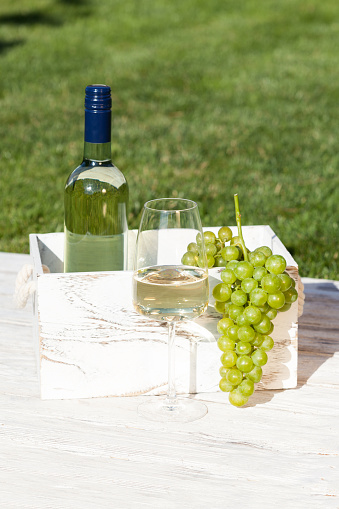 Wooden box with bottle of white wine and wineglass and grapes on wooden rustic table