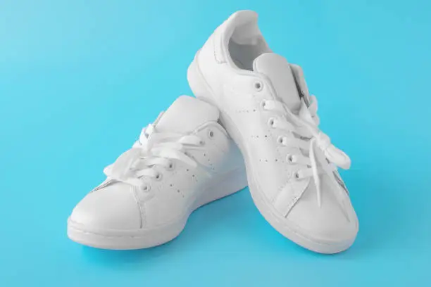 Photo of Pair of new white sneakers on blue background. New white leather sneakers sports shoes.