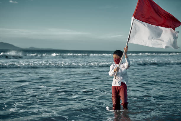 istock Schoolboy holding Red and White Flag at the Beach 1266733554