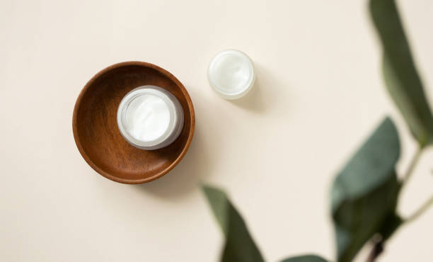 istock Open cream moisturizer jar in wooden plate on light beige background with blur eucalyptus leaf, above. Set natural organic eco cosmetic beauty products for skin and body care 1266734656
