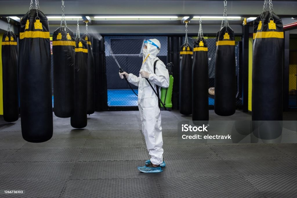 Gym employee wearing PPE and disinfecting everything A mid adult woman in protective gear disinfecting a gym. Cleaning Stock Photo