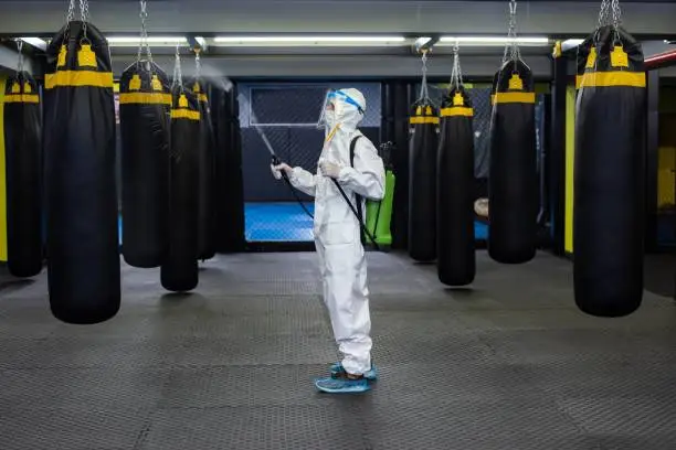 A mid adult woman in protective gear disinfecting a gym.