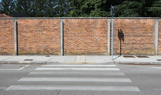 Surrounding brick wall, a concrete sidewalk, a crosswalk and a paved road ahead. Background for copy space