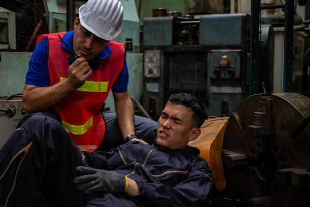 Asian man factory worker had a leg accident in working area with male supervisor talking on walkie talkie for help. el joven trabajador asiático tuvo un accidente en la pierna tirado en el suelo en la fábrica de tornos metálicos. supervisor de ingeniero hablando en walkie talkie para obtener ayuda. concepto de seguro industrial de fábrica y seguro de negocio.