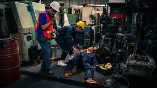 el trabajador asiático tuvo un accidente inconsciente en el suelo de la fábrica de tornos metálicos. supervisor de ingeniero masculino hablando en walkie talkie para obtener ayuda. concepto de seguro industrial y empresarial de fábrica. - accident occupation physical injury construction fotografías e imágenes de stock