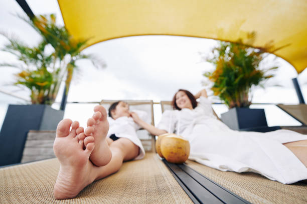 Positive mother and daughter lying on chaise-lounges, talking and drinking coconut water, focus on feet