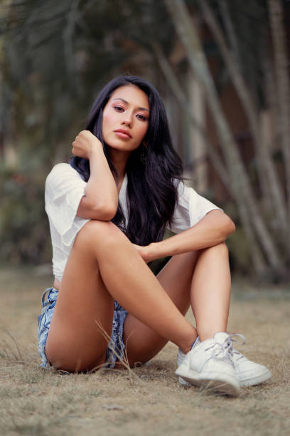 Beautiful Asian woman seats on grass, wearing jeans shorts, smiling enjoy weekends stock photo