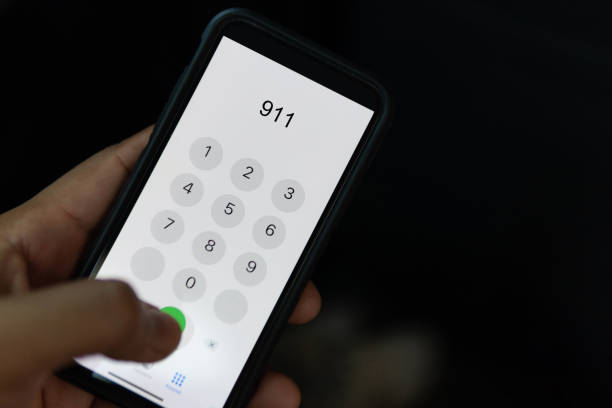mano sosteniendo el teléfono celular con el número de emergencia 911 sobre fondo negro - marcar usar el teléfono fotografías e imágenes de stock