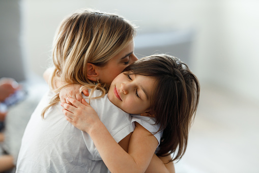 The young happy mother hugs her daughter on the floor of their apartment.