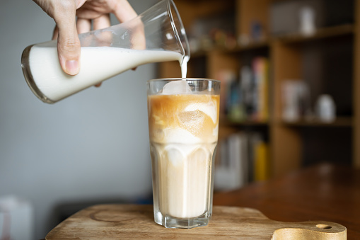 Pouring fresh milk into a glass of iced coffee