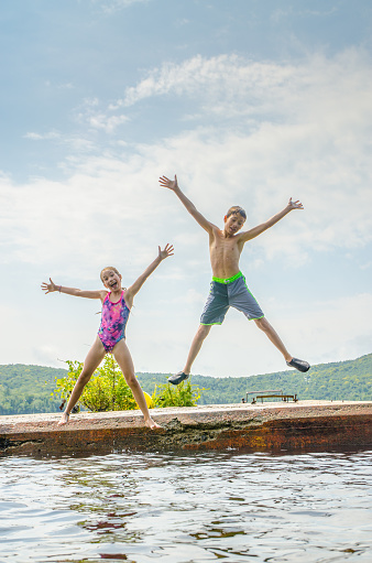 Boy and girl plunging in water lake from the deck during summer day vacations