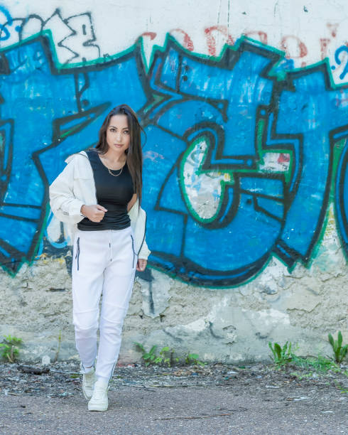 istock Young girl in a white tracksuit against a wall background with multicolored graffiti 1266751726