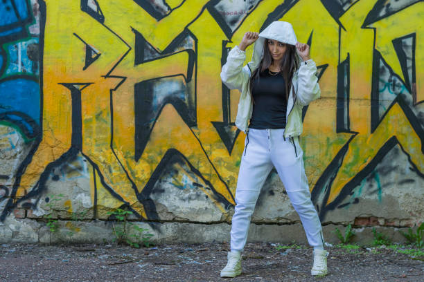 istock Young girl in a white tracksuit against a wall background with multicolored graffiti 1266751727