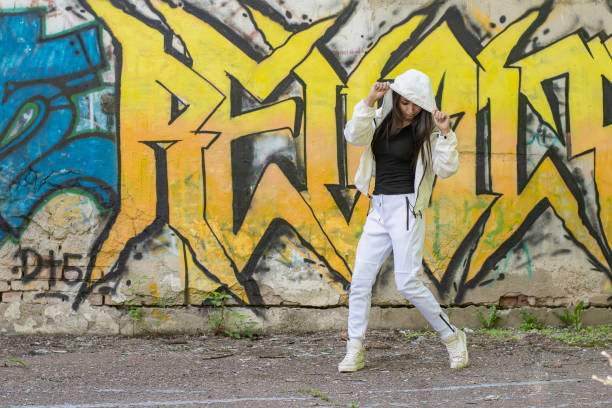 istock Young girl in a white tracksuit against a wall background with multicolored graffiti 1266751731