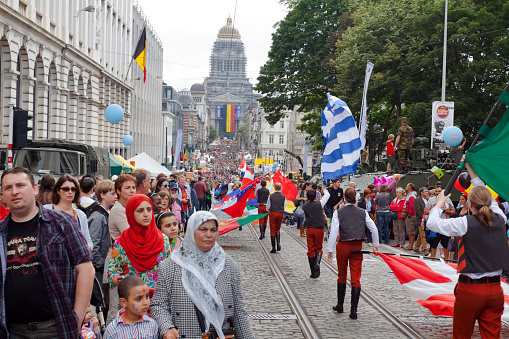 Flag parade in crowd in Brussels at national holiday. Scene is on street Rue de la Regence. In foreground some muslim people are walking. In background is huge Palace of justice