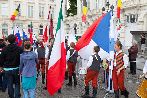 Young people in costumes for flag parade at national holiday in Brussels at square Place Royale. Group is entering square and walking through crowd for starting flag parade
