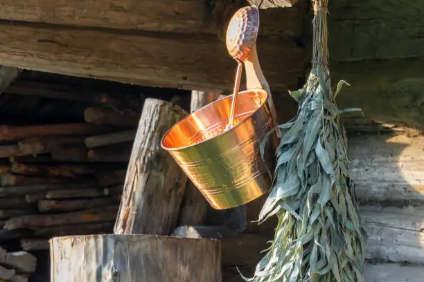 Sauna equipment background of wet copper bucket, ladle and bathing eucalyptus broom hanging in front of barn wall with copy space