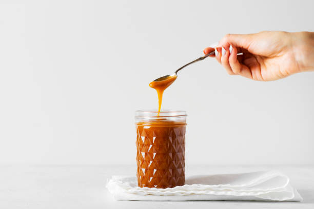 Liquid brown caramel in glass or jar with spoon on white background