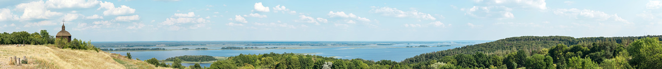 Panorama landscape of beautiful view of the Dnieper river with wooden chapel, forest and blue sky with clouds in Vitachov, Ukraine. National park Horodyshche Novgorod-Svyatopolche. Historical landmark