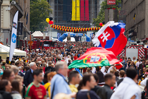 In crowd of people at belgian national day in Brussels. Scene is in street Rue de la Regence close to Palace of Justice in background with belgian flag at facade. In crowd is flag parade