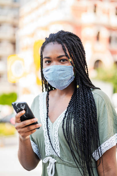 istock Young woman wearing protective face mask walking through city, using smart phone 1266758681