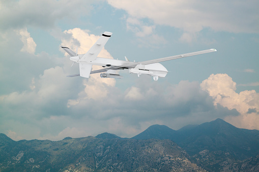 unmanned RC military drone flies over mountains with white clouds on a blue sky background