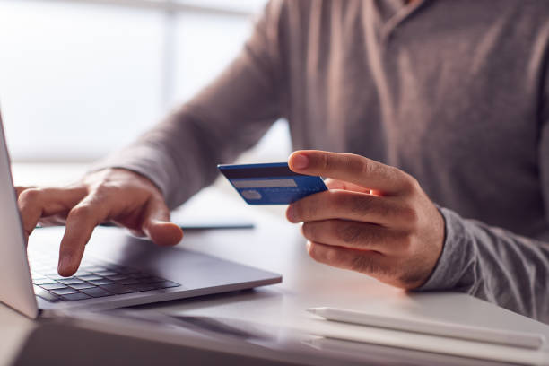 primer plano de empresario que trabaja tarde en el ordenador portátil en el escritorio haciendo pago en línea con tarjeta de crédito - pagar fotografías e imágenes de stock