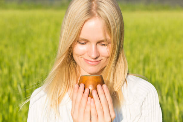 donna felice che beve una deliziosa bevanda alla tisana da una tazza di legno in verde naturale all'aperto. salute e benessere alternativi. - alternative medicine mortar and pestle herbal medicine herb foto e immagini stock