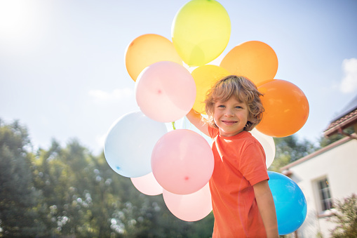 Small four years old boy playing with colorful balloons outside.