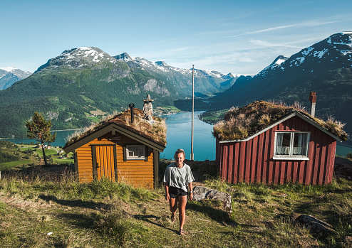 Woman walking against camera by fjord and cabins by Lovatnet/Raksetra, Norway.