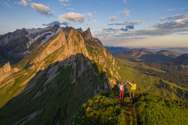 Couple hiking on mountain ridge looking at spectacular view in Appenzellerland Canton, Switzerland.\nDrone point of view