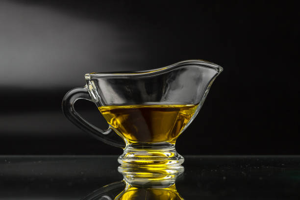 olive oil in a glass gravy boat. vegetable oil on a black background. vegetable oil on a black background. olive oil in a glass gravy boat. olive oil pouring antioxidant liquid stock pictures, royalty-free photos & images