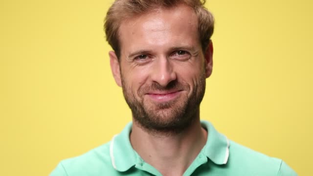 close up of sad young casual guy starting smiling and laughing on yellow background