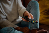 Closeup of young female hand holding remote control and changing channel at home watching television alone