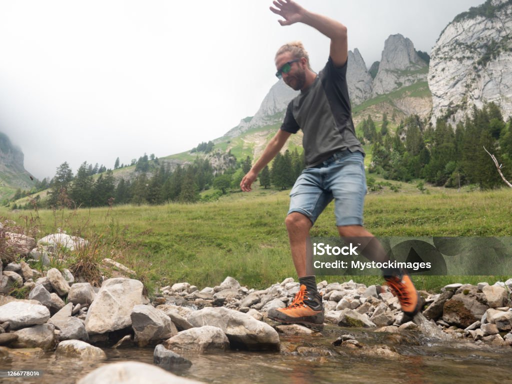 Hiker jumping over river Happy healthy man hiking on mountain trail in Summer enjoying nature and outdoor activities. Hiker jumps over river Jumping Stock Photo