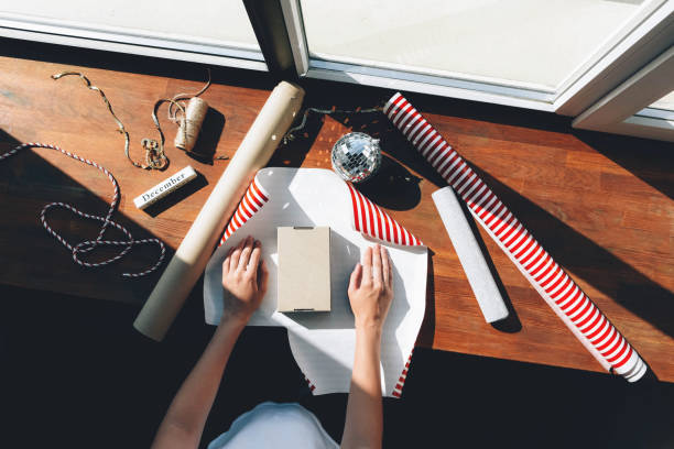 The girl is packing gifts near a large window. The girl is packing gifts near a large window. New Year's and Christmas. Stages of gift wrapping. person holding frame over face stock pictures, royalty-free photos & images