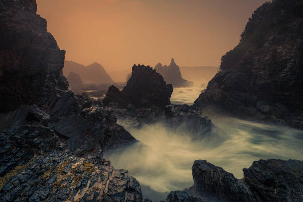 nebbia marina mistica, spruzzo di mare e alba sulla roccia vulcanica affilata - flowing nature spray rock foto e immagini stock